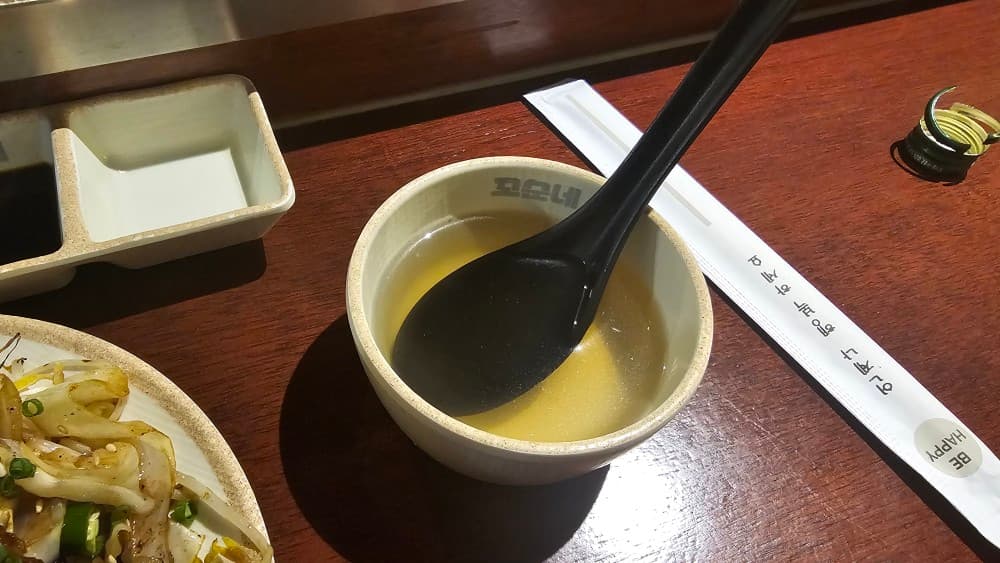 꼬순네 로고가 새겨진 그릇에 담긴 따뜻한 국물과 숙주 요리. 혼술하기 좋은 아늑한 분위기.