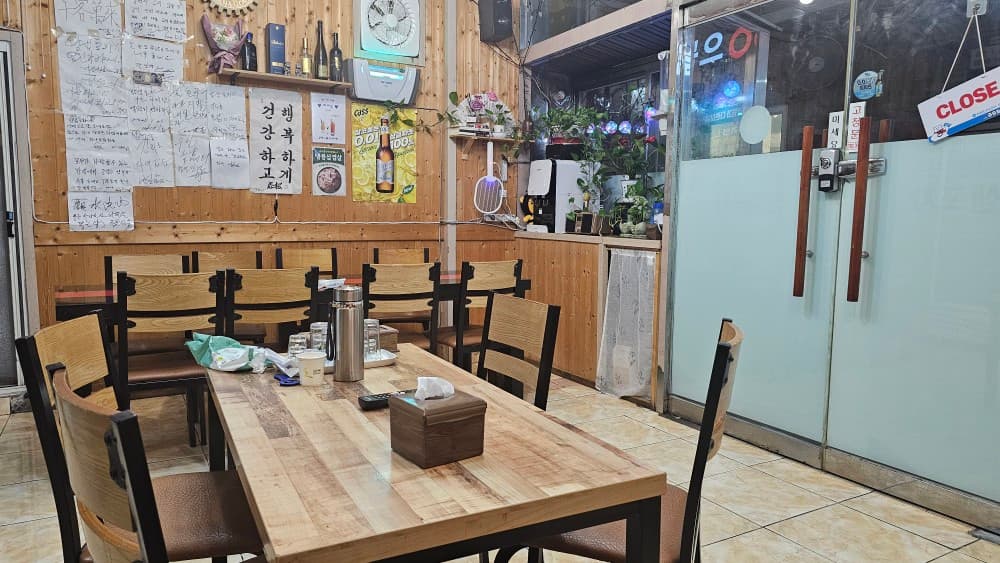 밤샘포차 내부의 따뜻한 목재 인테리어와 정겨운 벽면 낙서. 아늑한 테이블 좌석이 마련되어 혼술하기 좋은 부산 연산동 포차입니다.