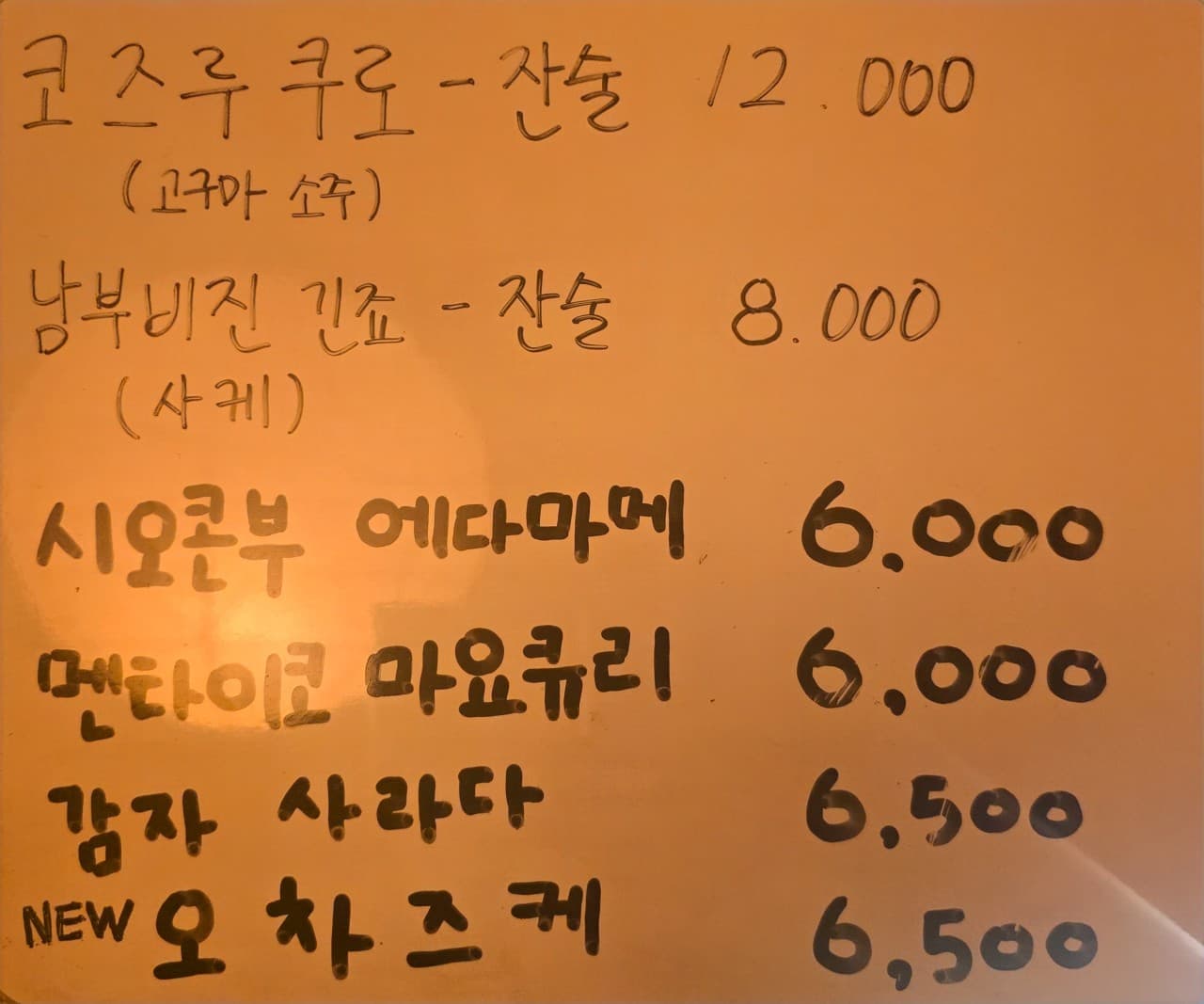 선술집 코코의 주황색 손글씨 메뉴판. 고구마 소주와 사케 잔술, 감자 사라다 등 혼술하기 좋은 가벼운 안주와 주류 메뉴를 보여줍니다.