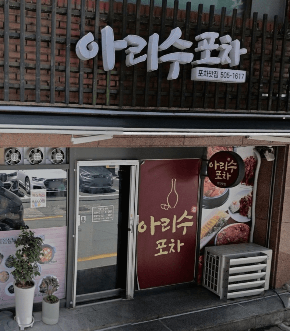 나무 격자 아래 흰색 간판과 술병 기호가 그려진 붉은색 시트지가 부착된 유리문 및 메뉴 사진이 있는 포차 입구