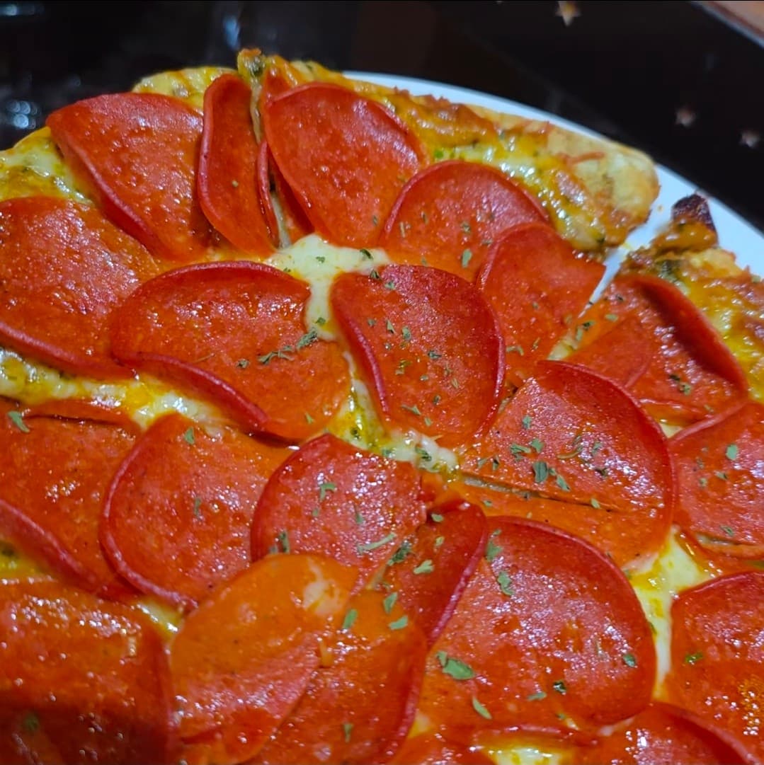 어두운 조명 아래 붉은 페퍼로니가 촘촘하게 깔린 피자와 녹아내린 치즈 위로 뿌려진 허브 가루