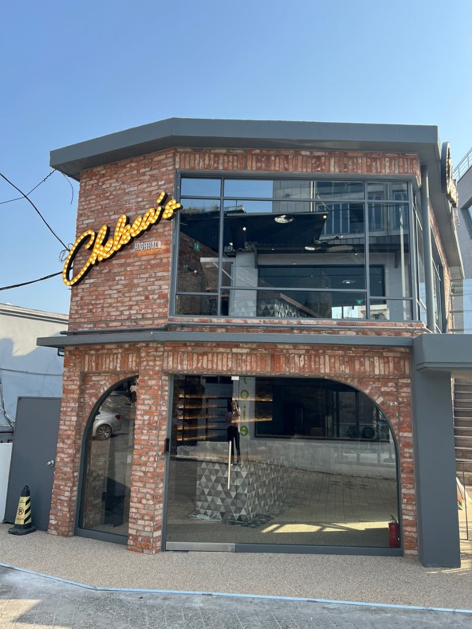 전구 조명 간판이 달린 붉은 벽돌 건물 외관과 유리창 너머로 보이는 1인용 바 테이블 좌석