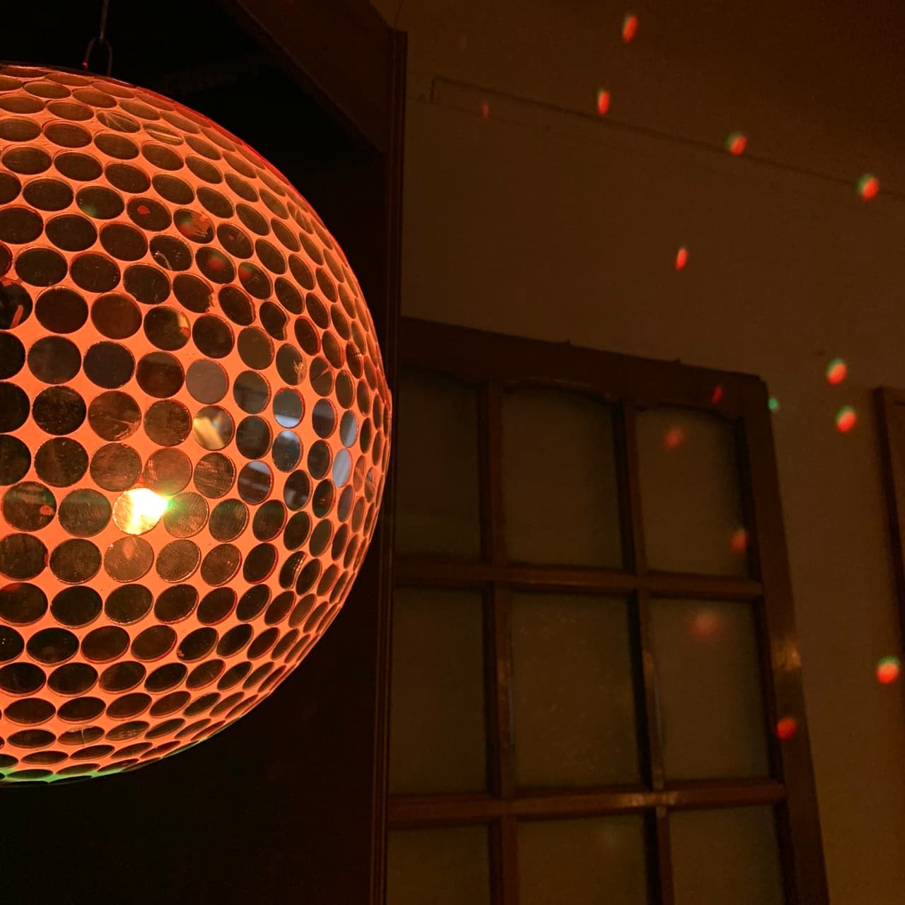 주황색 조명이 들어온 미러볼과 벽면에 맺힌 붉은 빛망울 그리고 어두운 배경의 나무 격자 창문