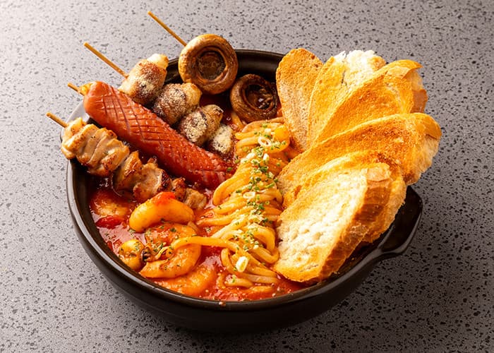 붉은 토마토 소스 면 요리와 바게트, 새우, 소시지 및 버섯 꼬치구이가 담긴 1인용 검은 그릇