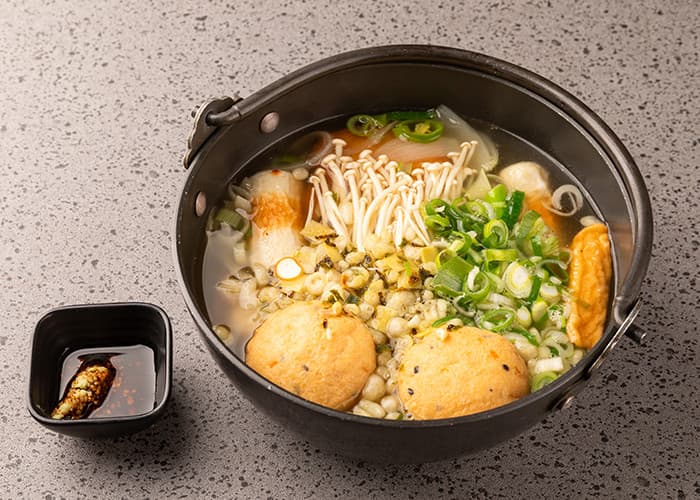 무쇠 냄비에 담긴 여러 종류의 어묵과 팽이버섯, 송송 썬 대파와 와사비를 곁들인 1인용 간장 종지