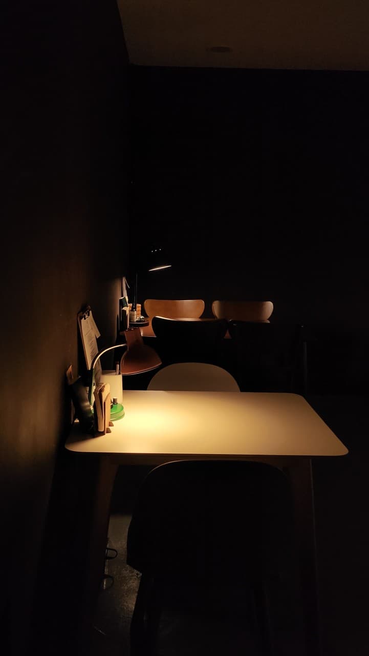 어두운 벽면을 배경으로 개별 스탠드 조명이 하얀 테이블을 집중적으로 비추는 1인용 좌석 전경