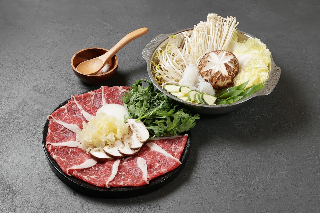 어두운 회색 바탕에 놓인 금속 냄비 속 배추와 버섯, 둥근 접시에 가지런히 펼쳐진 소고기와 나무 수저 세트