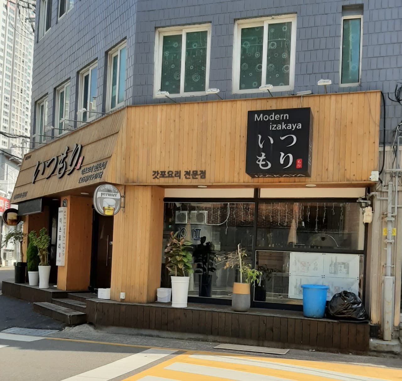 회색 벽면 아래 목재로 마감된 외관과 통유리 너머로 보이는 1인용 바 테이블 전경