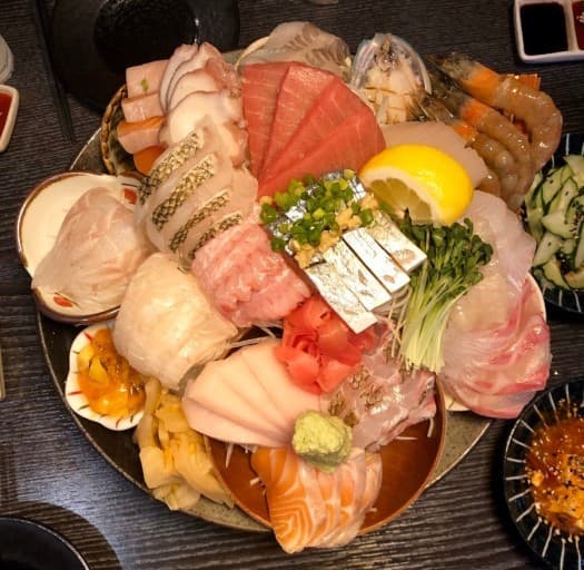 검은색 테이블 위 참치와 연어, 새우 등 다양한 종류의 생선회가 담긴 1인용 모둠 사시미 플레이트