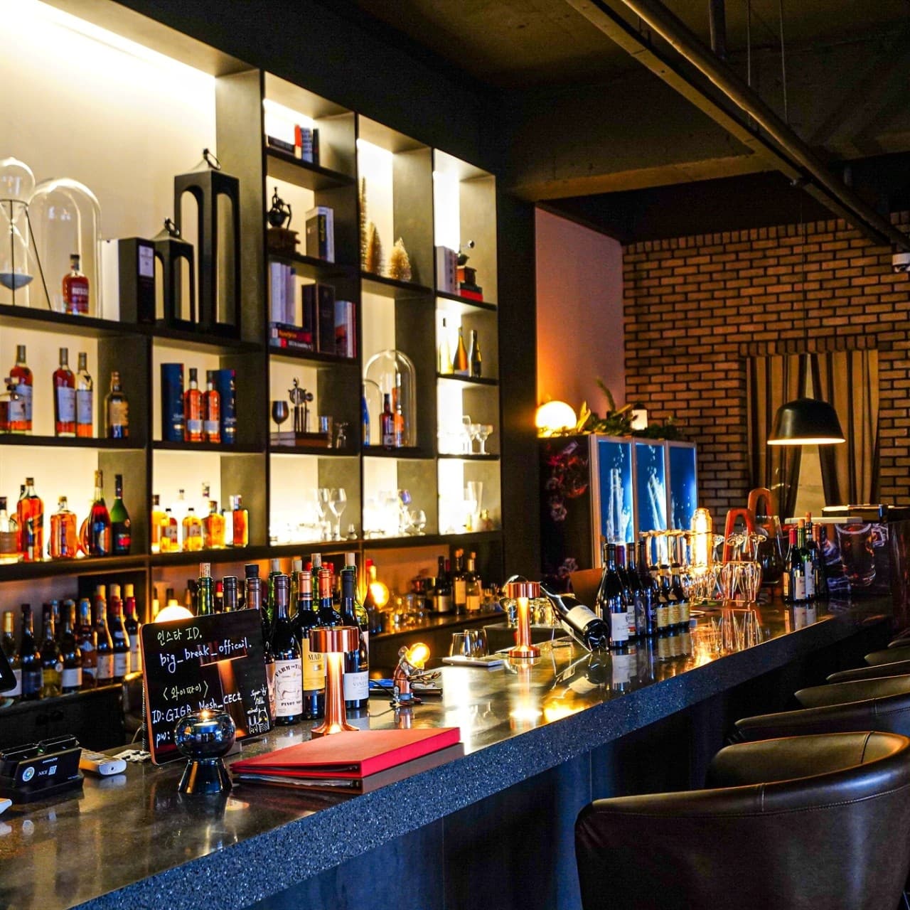 어두운 실내 속 노란 조명이 비추는 바 카운터와 가죽 의자 및 주류가 진열된 벽면 선반