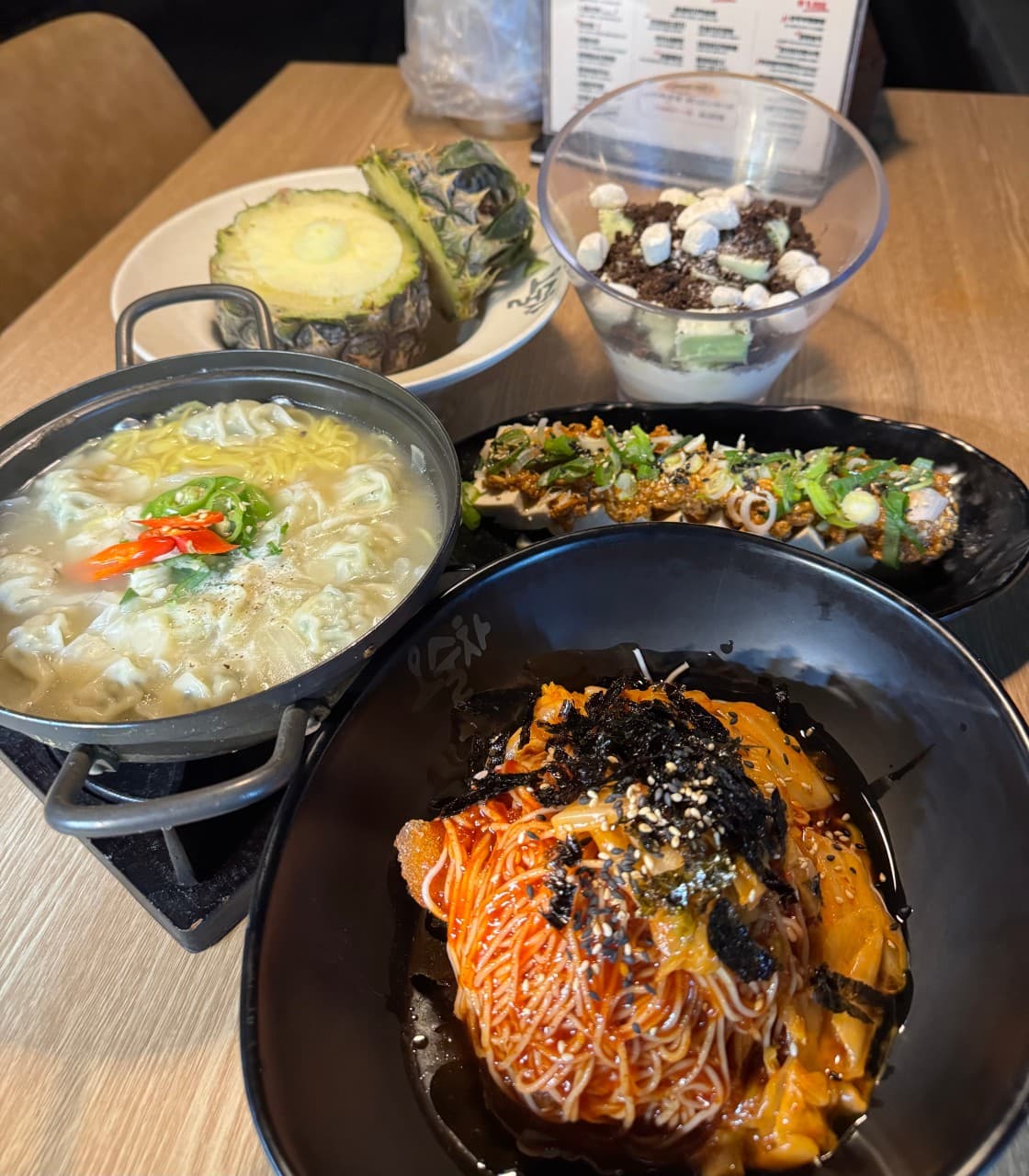 비빔국수와 만두전골, 파인애플 등 소량씩 담긴 여러 안주가 차려진 1인용 목재 테이블 위 상차림