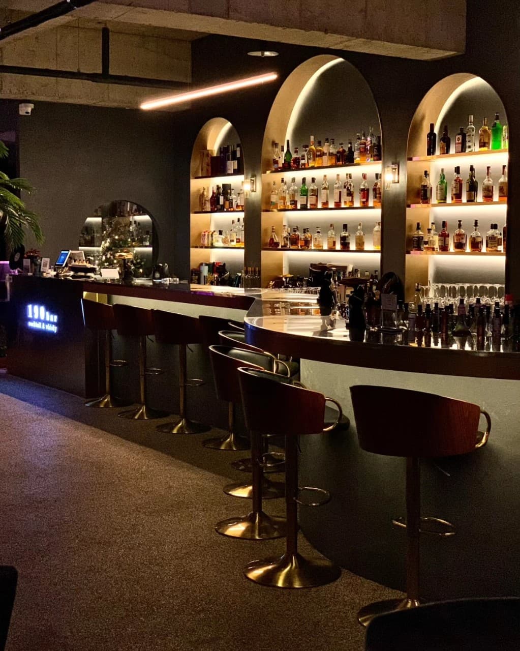 아치형 선반에 진열된 술병들과 간접 조명이 비치는 곡선형 바 테이블에 놓인 1인용 좌석