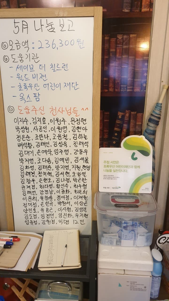 기부금액과 명단이 적힌 화이트보드와 지폐가 담긴 투명 모금함, 후원 안내판이 나란히 비치된 매장 한 켠의 선반 전경