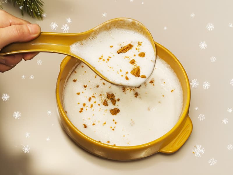 노란색 도자기 사발에 가득 담긴 흰 거품과 갈색 토핑을 국자로 뜨는 모습. 1인용 식기 위로 눈꽃 무늬가 겹쳐진 시각적 구성.