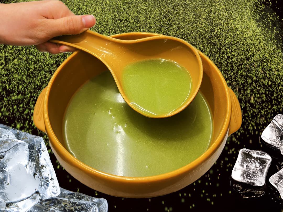 갈색 항아리 용기에 가득 담긴 초록색 막걸리와 국자, 주변을 장식한 각얼음과 초록색 가루 입자