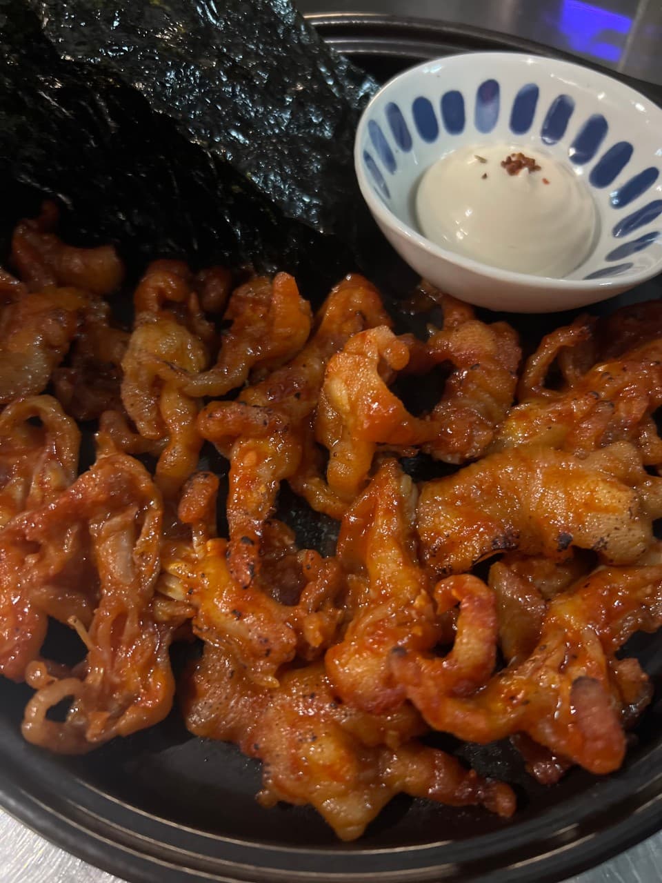 어두운 조명 아래 금속 테이블 위 붉은 양념 닭발과 조미 김 그리고 마요네즈 소스가 담긴 종지