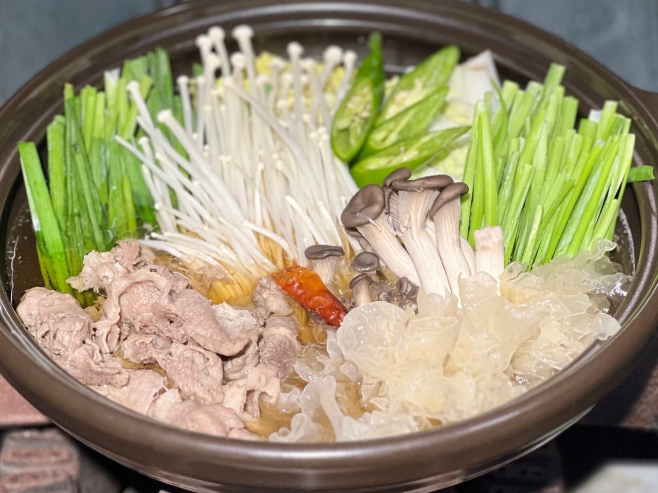 갈색 전골 냄비에 얇게 썬 고기와 흰 목이버섯, 팽이버섯, 부추, 청양고추를 가지런히 담아낸 1인용 전골 요리