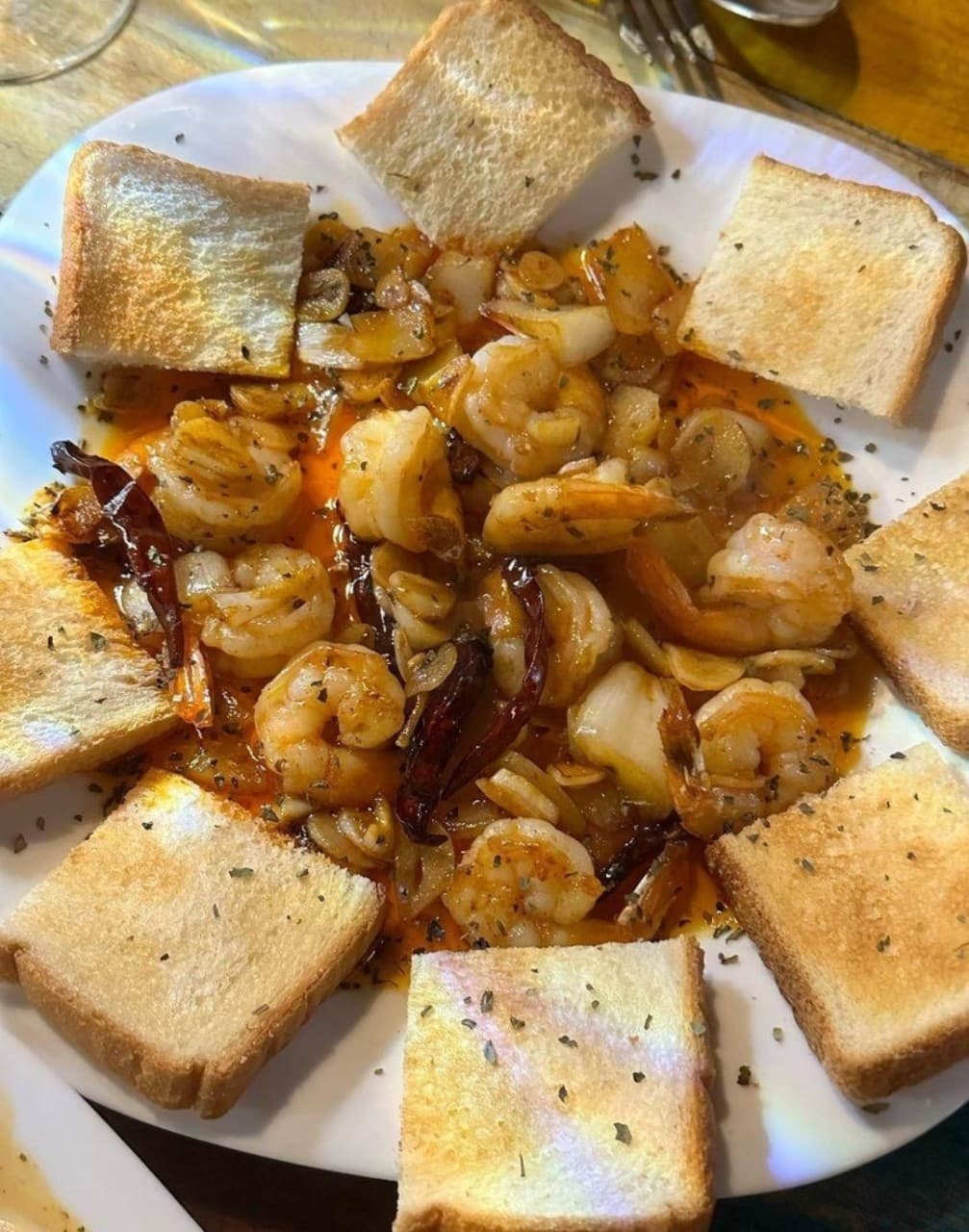 마늘 슬라이스와 건고추를 넣은 오일 소스 새우 요리와 접시 가장자리에 놓인 구운 식빵 조각들