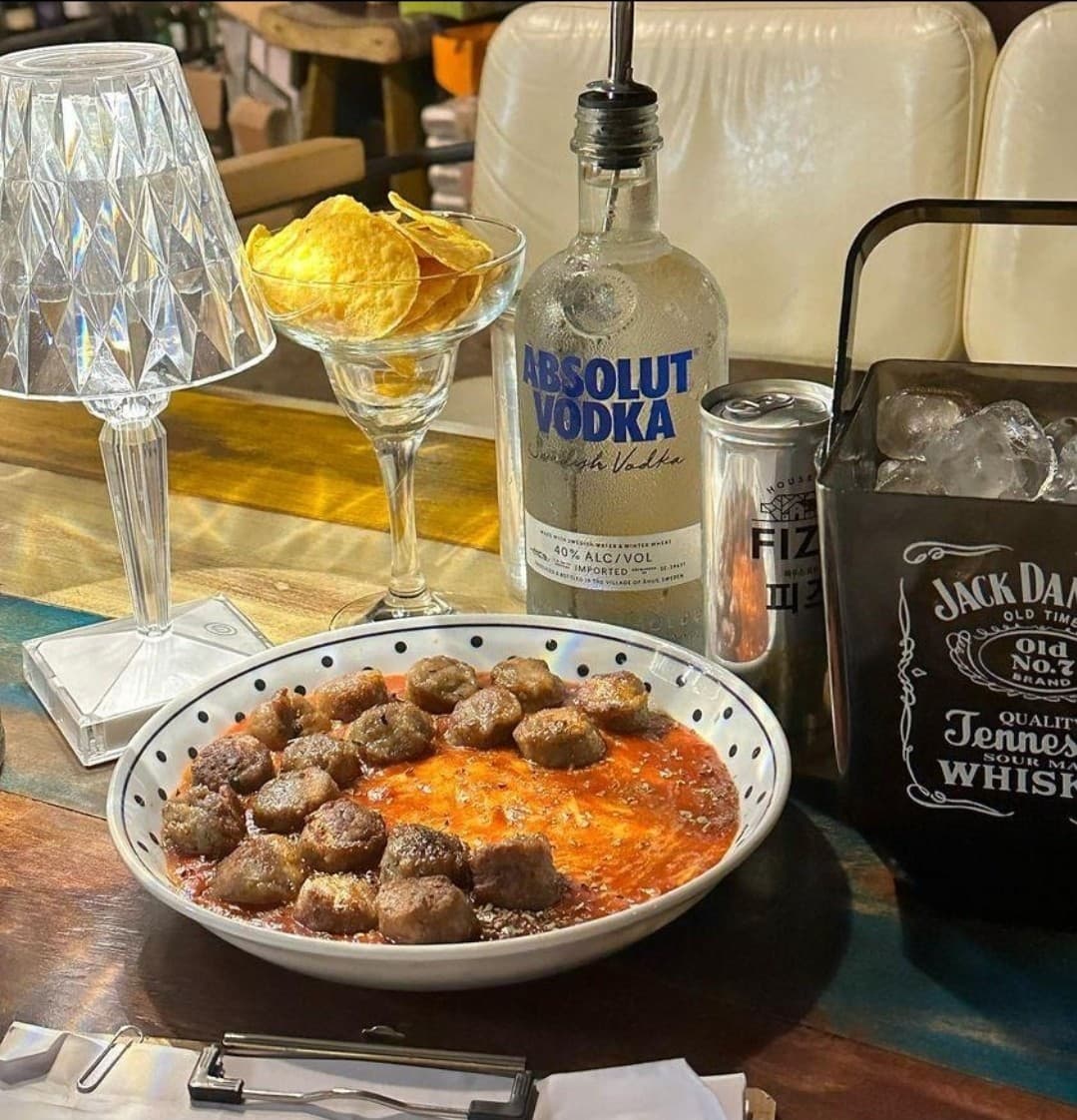 조명이 켜진 1인용 바 테이블 위 미트볼 접시와 나초, 보드카 병과 얼음이 담긴 아이스 버킷