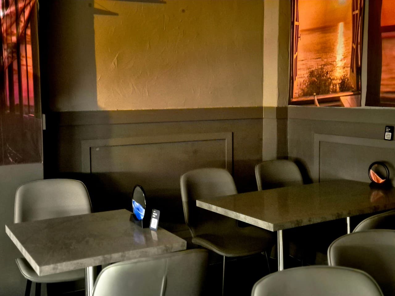 주황색 조명이 비치는 벽면 아래 배치된 소규모 인원용 테이블과 의자. 벽면의 일몰 풍경물과 테이블 위 원형 모래 소품