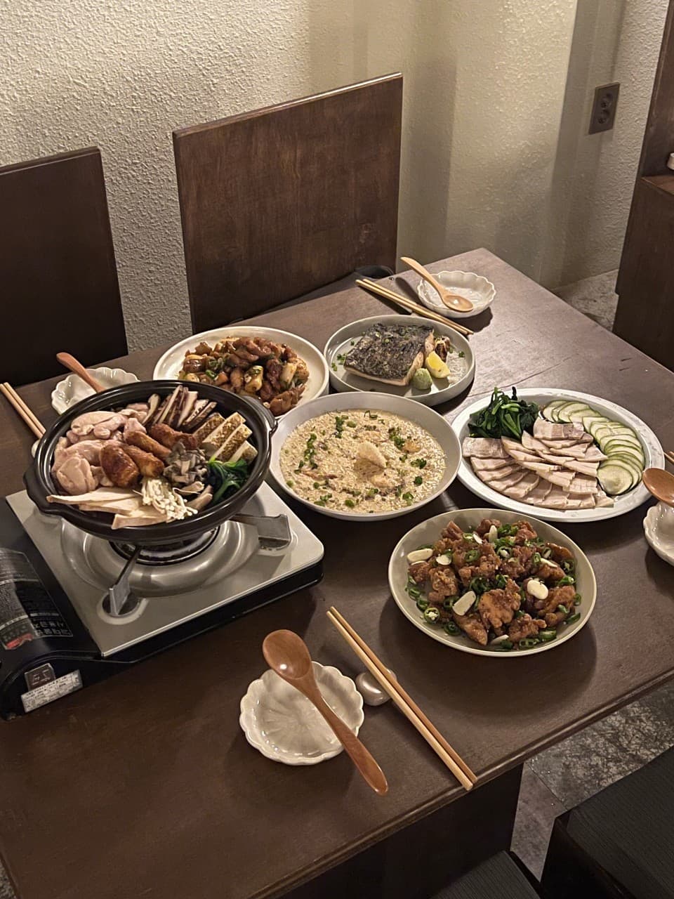 어두운 조명 아래 목재 테이블 위 가스버너에 올린 전골과 여러 안주 접시 및 1인용 나무 수저