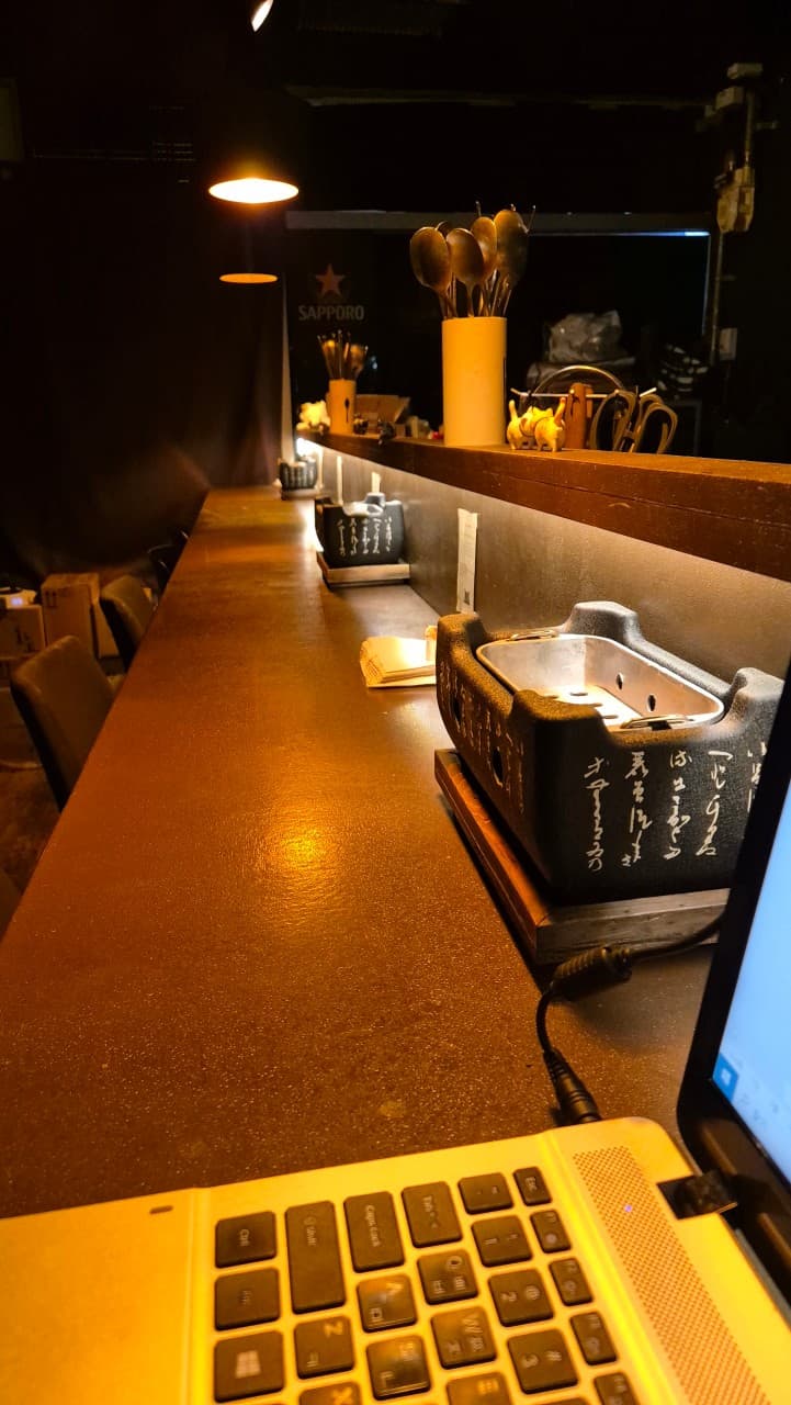 어두운 실내 주황색 핀 조명이 비추는 긴 카운터 테이블 위 1인용 미니 화로와 노트북 키보드