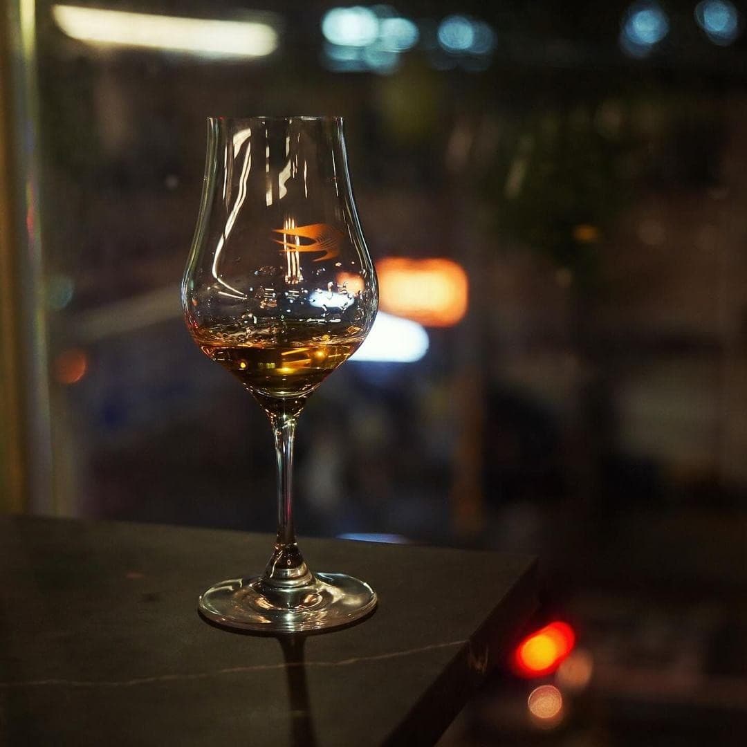 어두운 밤 창가 테이블 위 호박색 위스키가 소량 담긴 잔 하나와 흐릿하게 퍼지는 거리의 조명