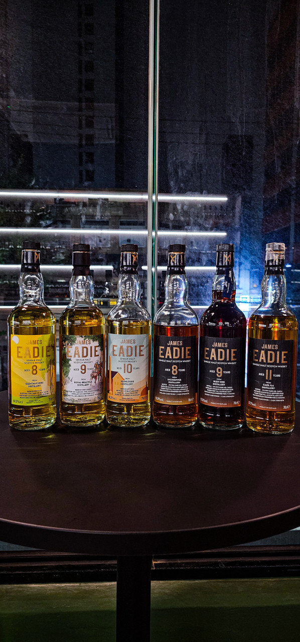 어두운 밤 창가 원형 테이블 위에 나란히 세워진 위스키 병들과 유리창에 비친 건물 불빛