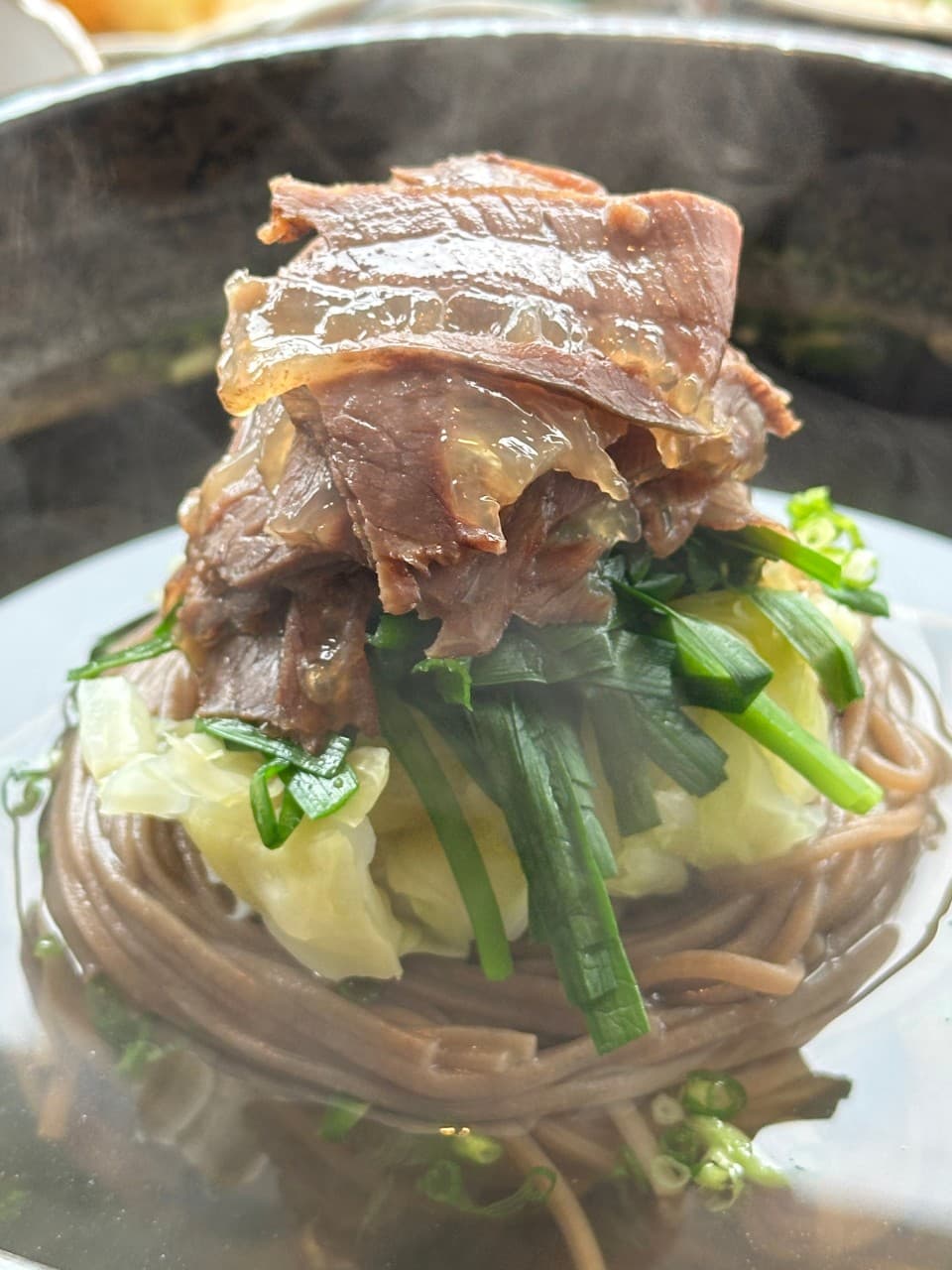 김이 올라오는 맑은 육수 속 메밀면과 양배추, 부추 위로 얇게 썬 고기가 층층이 쌓인 1인용 메뉴