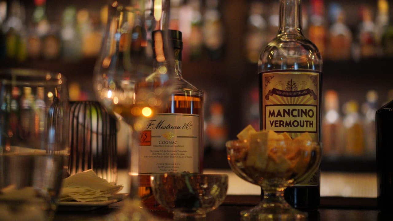 낮은 조도의 카운터 테이블 위 코냑과 베르무트 병, 1인용 안주가 담긴 작은 유리 볼