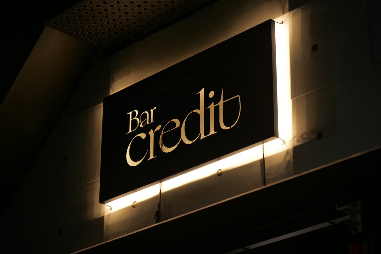 어두운 밤 노출 콘크리트 외벽에 부착된 검은색 사각 간판과 글자 뒤편에서 새어 나오는 노란색 조명