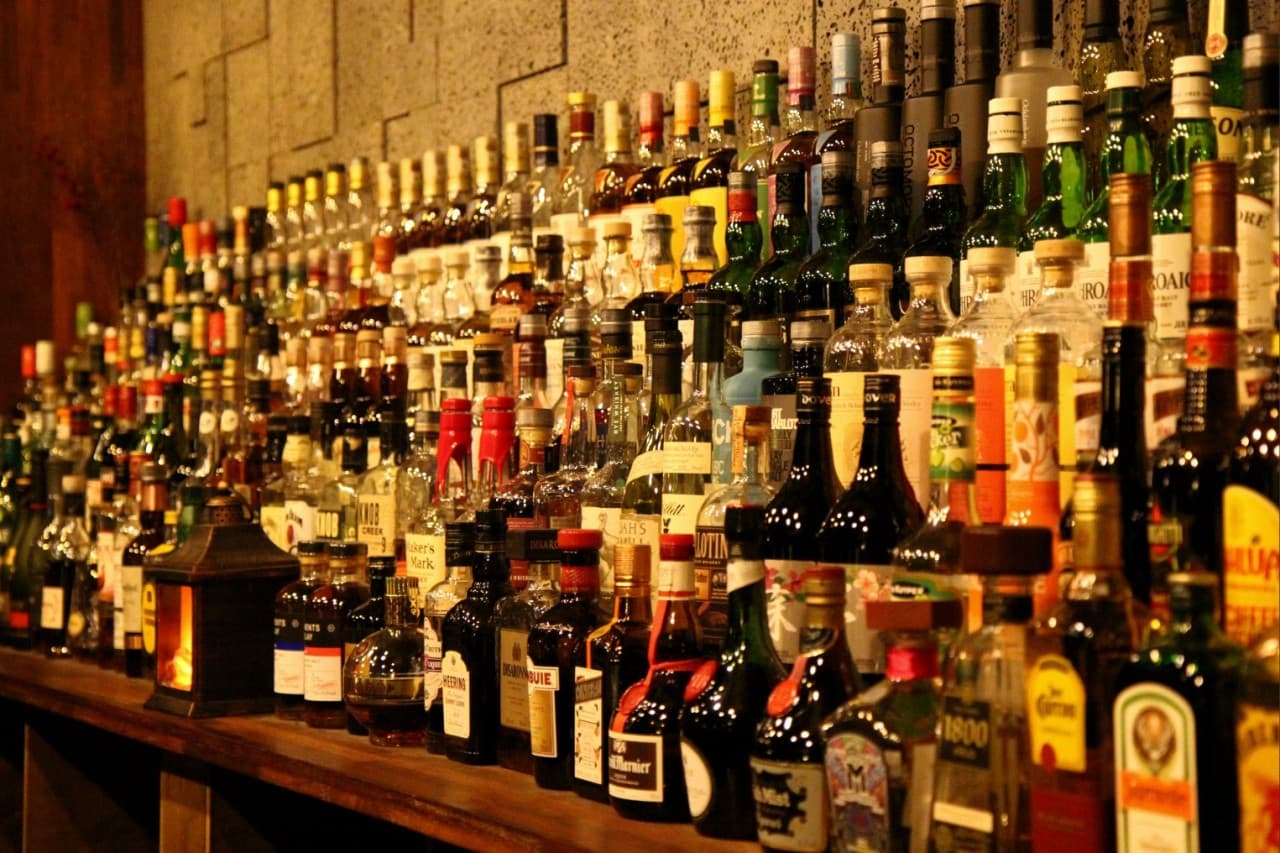 어두운 실내 황색 조명 아래 목재 카운터 뒤편으로 촘촘히 진열된 위스키 병들과 테이블 위 작은 등불