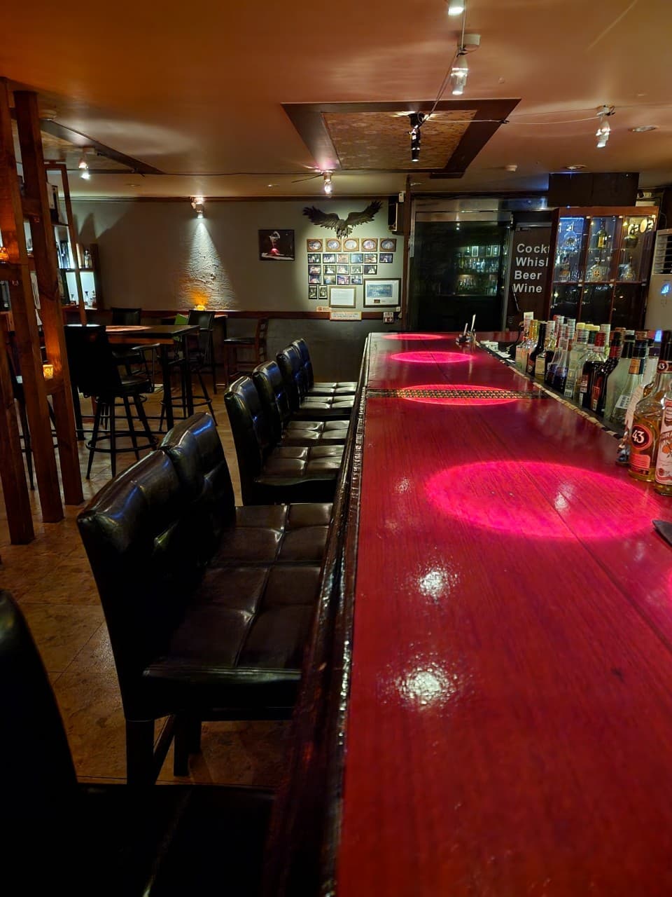 붉은색 원형 조명이 비치는 긴 목재 카운터와 1인용 검은 가죽 의자가 나란히 배치된 공간