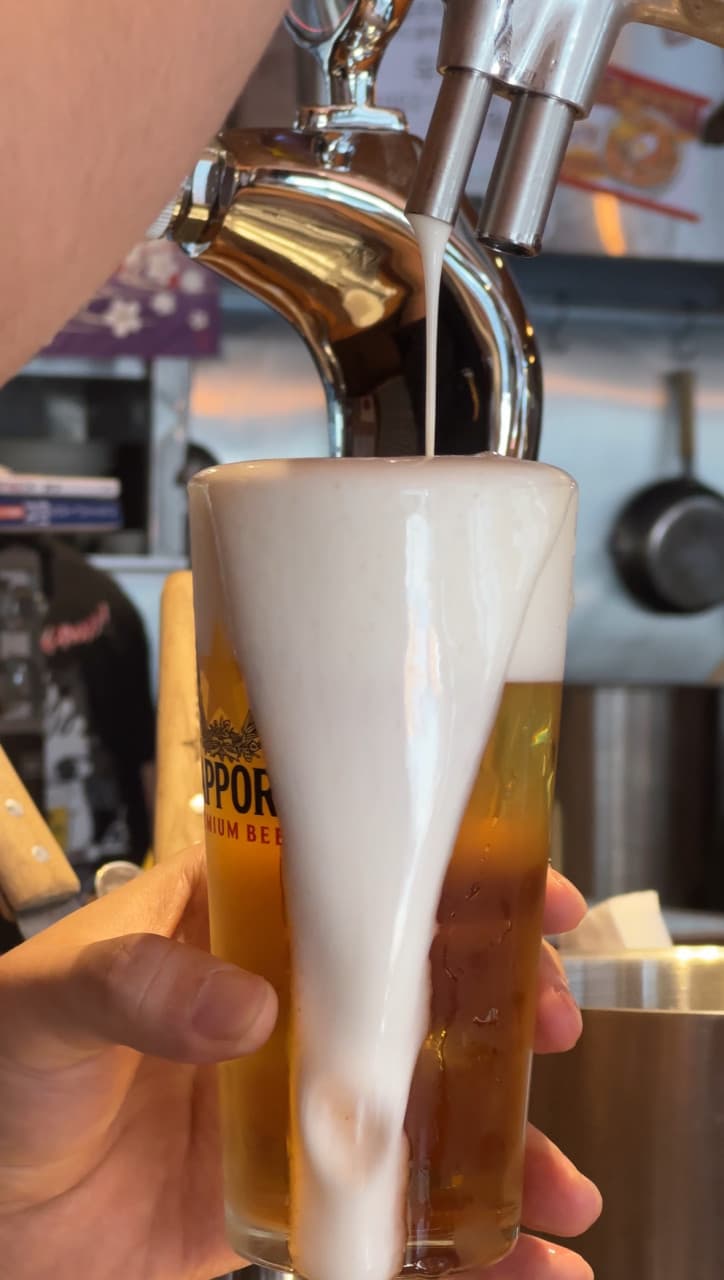 금속 생맥주 탭에서 유리잔에 담기는 맥주와 잔 위로 수북하게 쌓여 넘쳐흐르는 조밀한 흰 거품