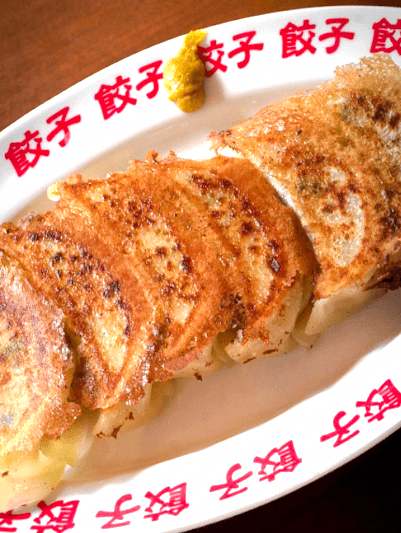 붉은색 한자가 테두리에 적힌 흰색 접시 위 바삭하게 구워진 1인용 교자 만두와 노란 겨자