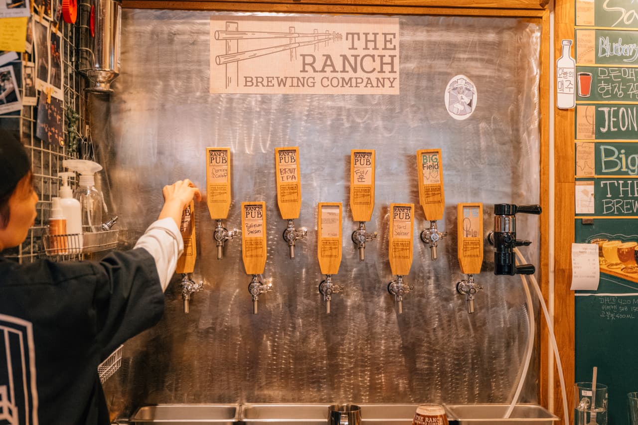 스테인리스 벽면에 나열된 목재 맥주 탭 핸들과 메뉴가 적힌 칠판이 배치된 바 테이블 공간