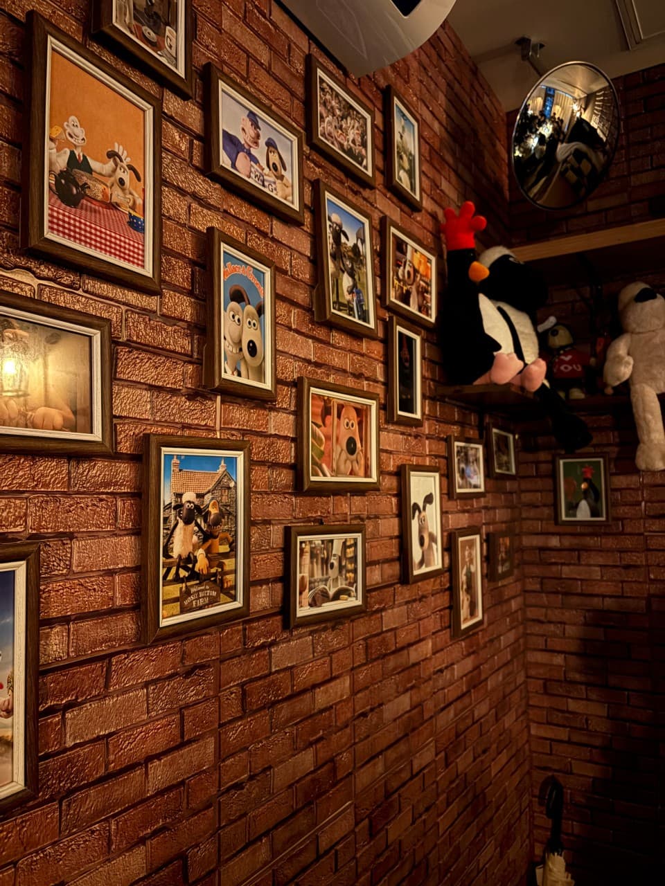 어두운 조명이 비치는 붉은 벽돌 벽면에 걸린 다수의 캐릭터 액자들과 선반 위 인형 및 상단 볼록 거울