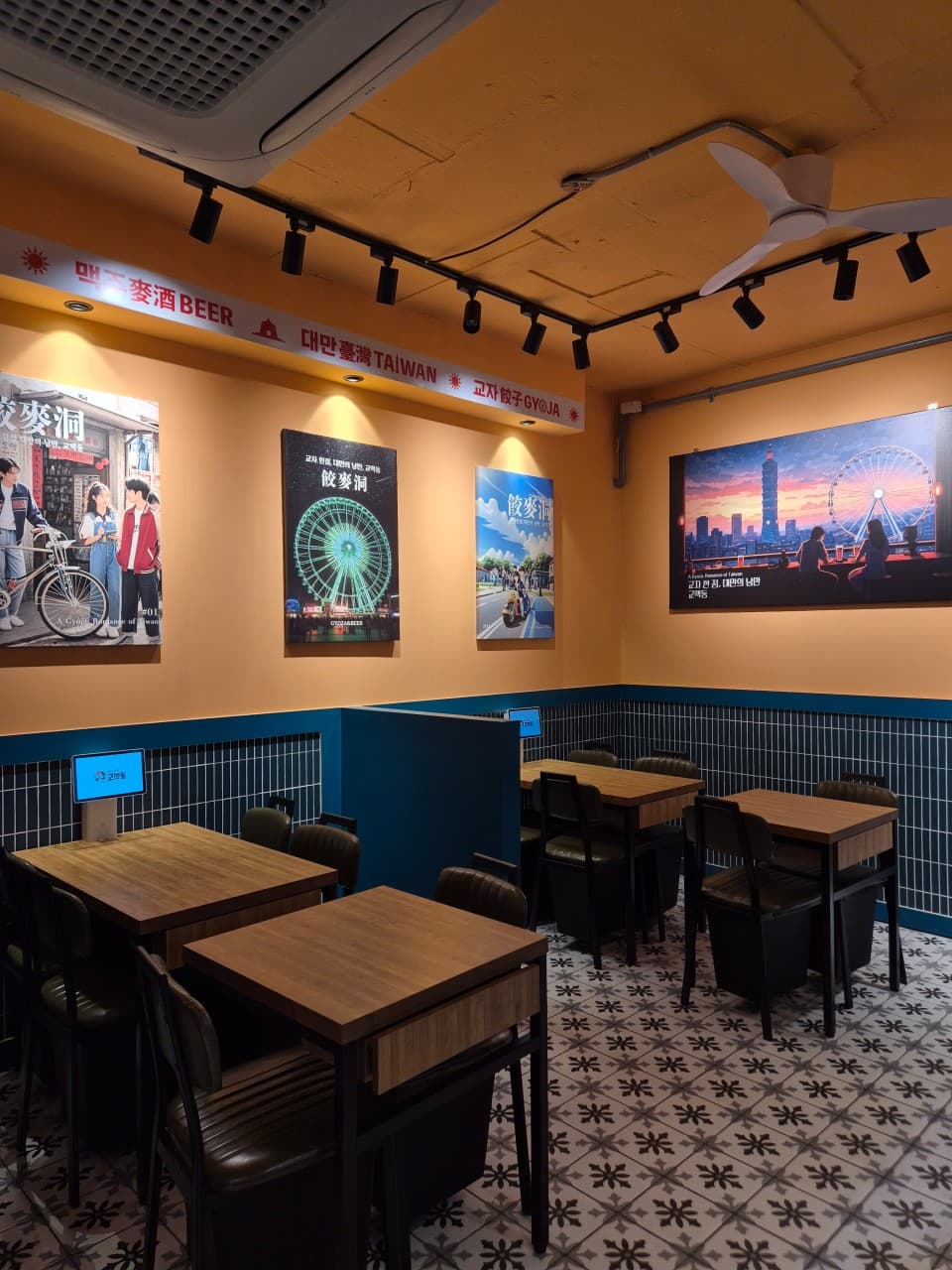 노란 벽면의 대만 풍경 포스터들과 개별 주문용 태블릿이 비치된 소형 목재 테이블, 패턴 타일 바닥이 보이는 내부 전경