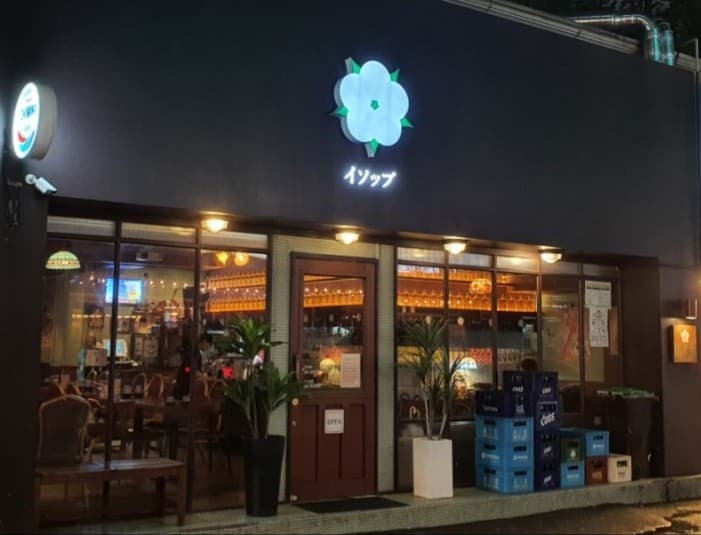 어두운 외벽에 꽃 모양 조명이 켜진 건물 외관과 유리창 너머 주황색 조명 아래 일렬로 배치된 바 테이블과 좌석