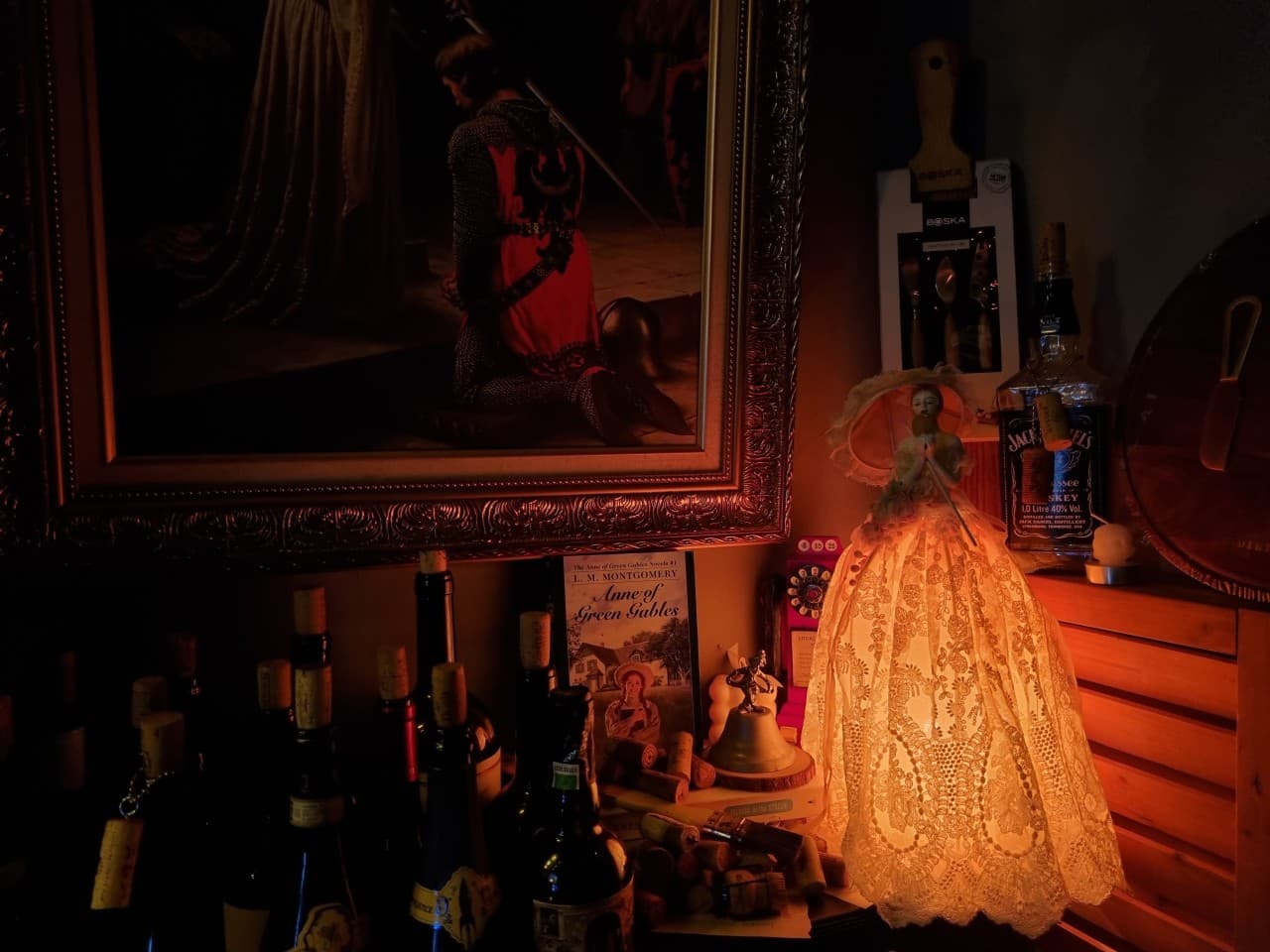 어두운 조명 아래 레이스 인형 스탠드와 고전적인 액자, 여러 병의 와인이 놓인 바 테이블 구석