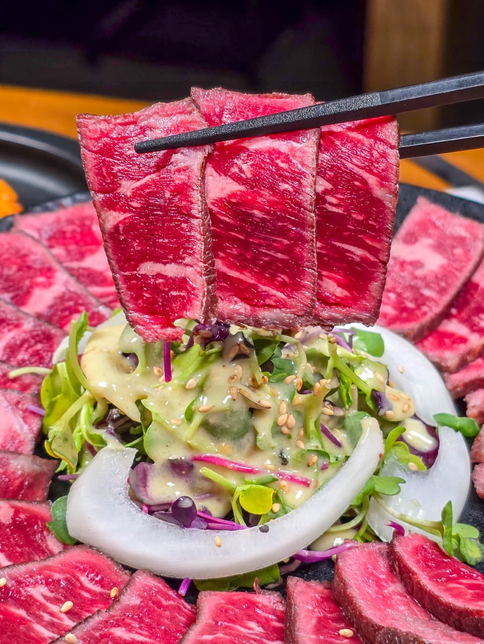 검은 젓가락으로 들어 올린 붉은 소고기 타타키와 채소 샐러드가 담긴 1인용 안주 접시