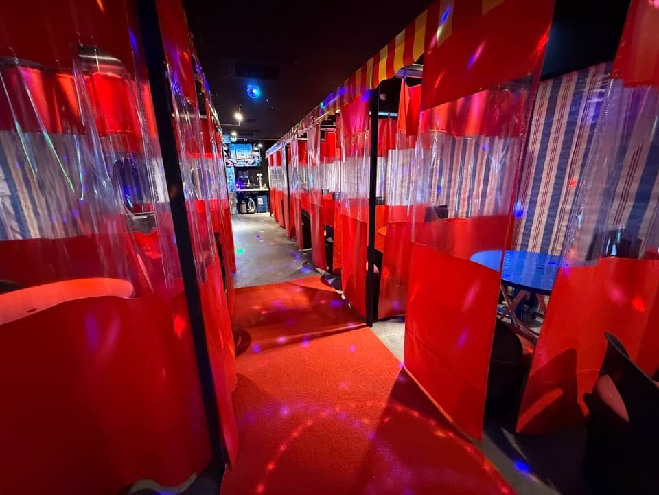 붉은색 비닐 천막으로 칸막이가 설치된 독립된 좌석 공간과 원형 테이블. 어두운 실내 통로와 바닥에 비치는 화려한 조명