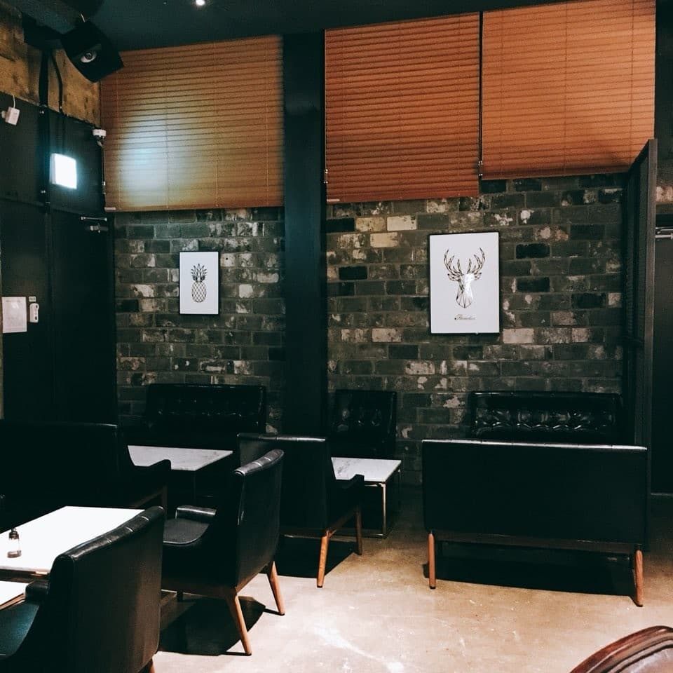 벽돌 벽 앞의 검은색 가죽 1인용 소파와 대리석 테이블이 배치된 실내. 목재 블라인드와 소형 액자가 걸린 어두운 톤의 좌석 공간