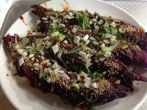 흰색 둥근 접시 위에 붉은 양념이 골고루 발린 생선 구이와 듬뿍 얹어진 다진 파와 참깨