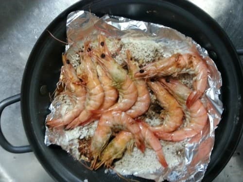 검은색 전골 냄비 속 은박지 위에 굵은 소금을 깔고 붉은 빛으로 익힌 새우들을 나란히 배치한 소금구이
