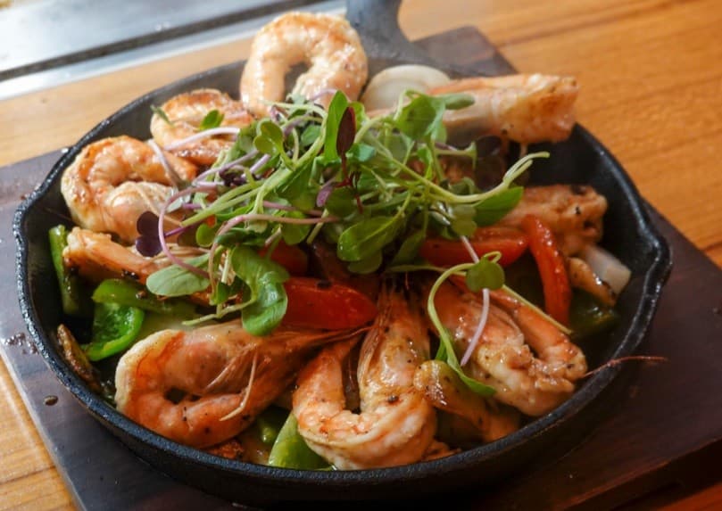 서울특별시 마포구 호요 홍대 이자카야 다찌석 조명 아래 무쇠 팬에 담긴 구운 새우와 어린잎 채소. 1인 혼술 상황에 적합한 철판 요리 구성.