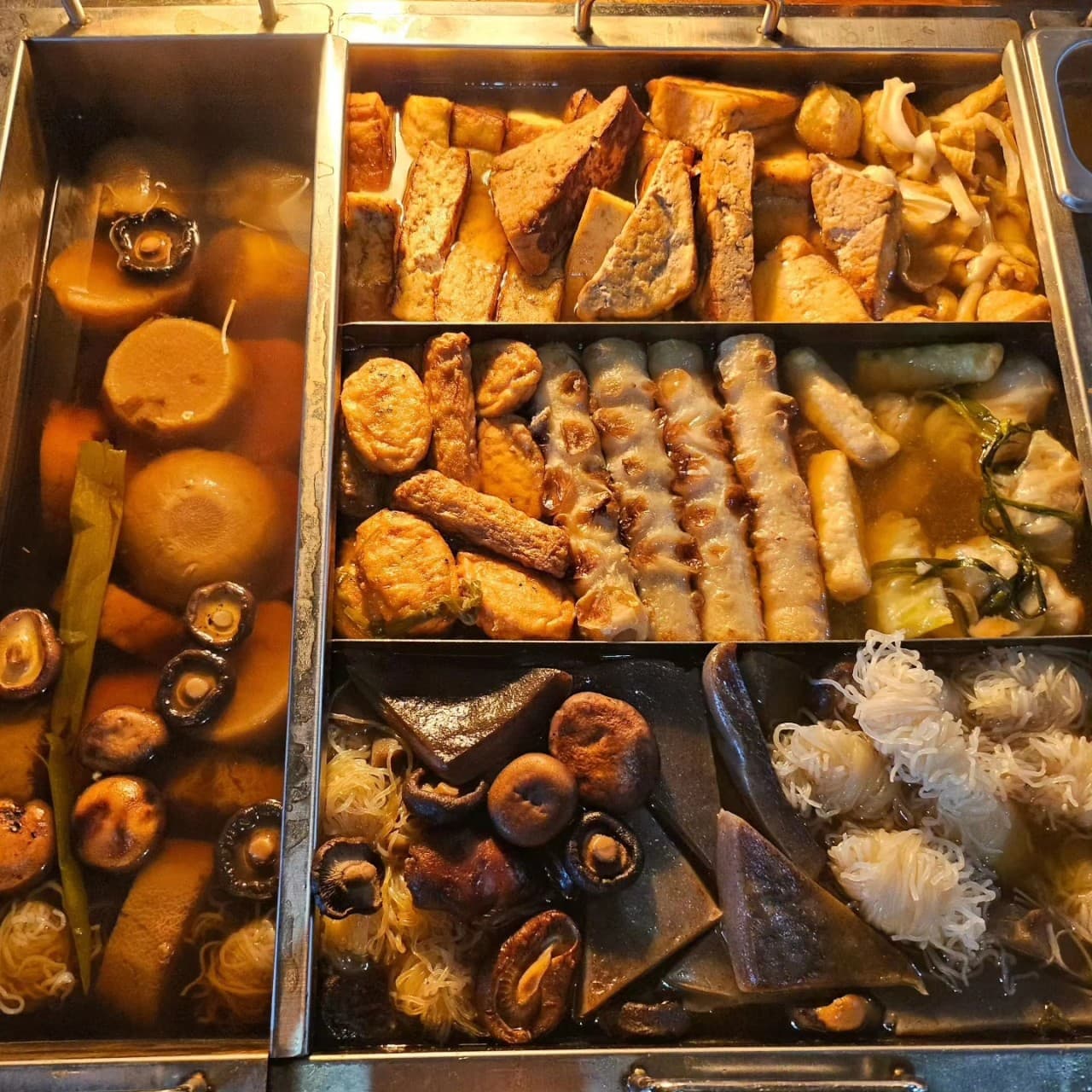 경기도 수원시 고래다 수원 장안 오뎅바 조명 아래 칸막이 냄비 속 무와 표고버섯, 여러 종류의 어묵이 담긴 1인 다찌석 혼술 현장. 식재료의 질감이 강조된 모습.