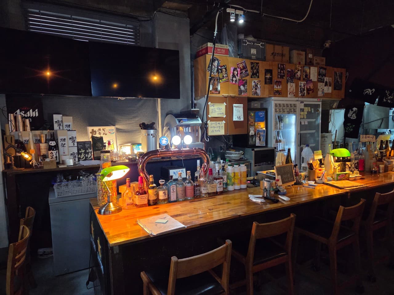 경기도 수원시 고래다 수원 장안 오뎅바. 오렌지색 조명 아래 배치된 1인 다찌석과 나무 테이블. 혼술 하기 적합한 긴 카운터 좌석과 진열된 주류 병들이 보이는 실내.