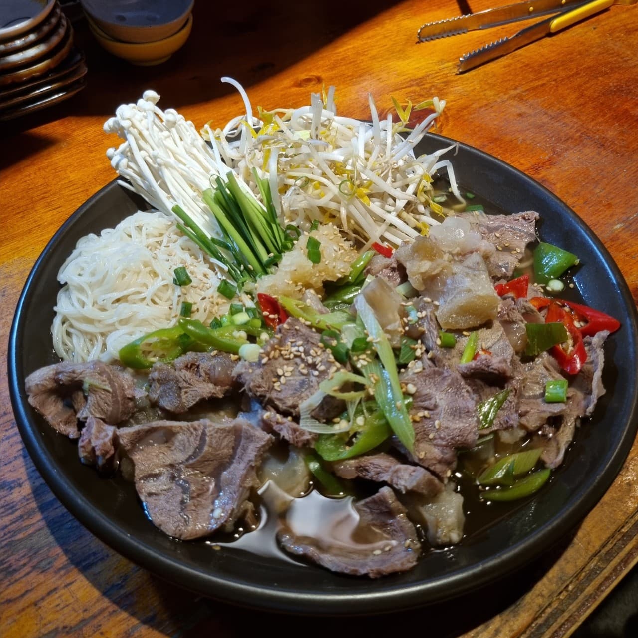 경기도 수원시 배씨상회 수원스타필드 요리주점 다찌석. 조명 아래 결이 살아있는 고기와 숙주, 소면이 담긴 그릇이 놓인 나무 테이블 위 1인 혼술 상황.