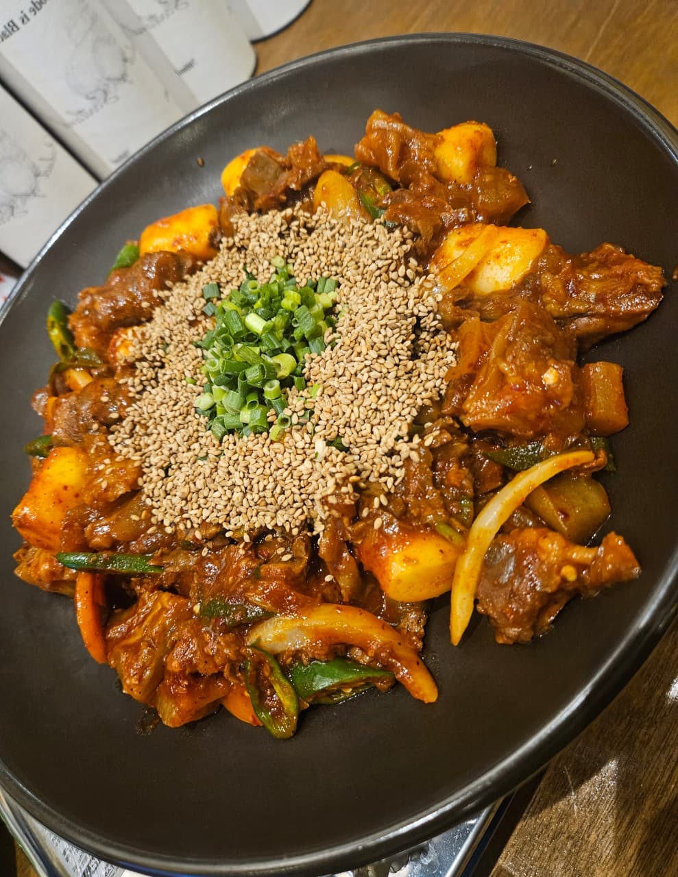 경기도 수원시 배씨상회 수원스타필드 요리주점 다찌석 1인 혼술. 나무 테이블 위 조명을 받은 고기 볶음 위로 깨와 쪽파가 가득 올라간 검은색 접시가 놓인 상황.